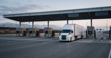Tractocamión de carga en carril comercial dedicado en un cruce fronterizo México–Estados Unidos al amanecer